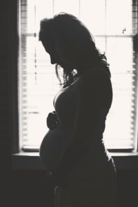 silhouette of a woman with her hands on her pregnant belly