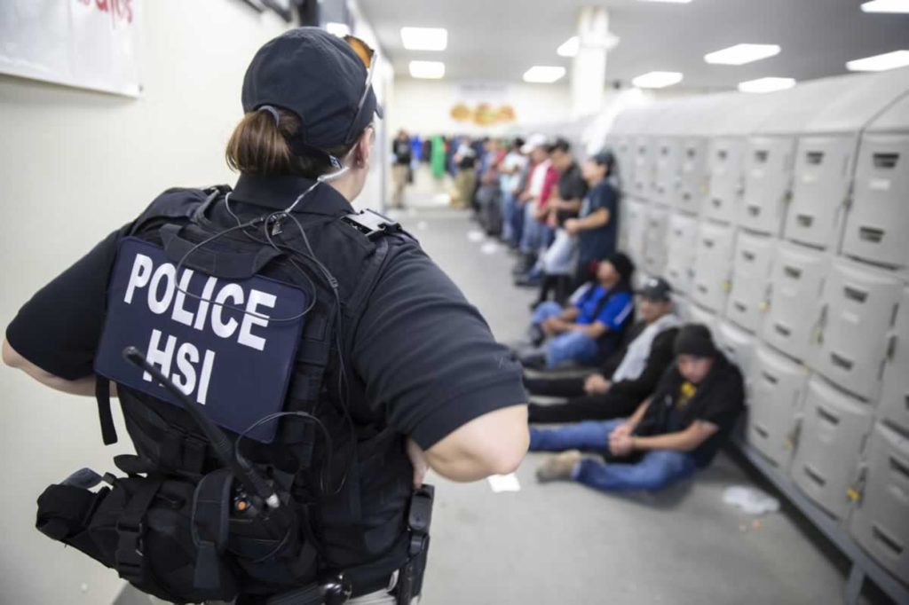 Image by Vox for police officer standing in front of a line of people bound sitting and leaning against a wall